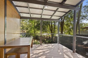 A covered outdoor area with a wooden table and chairs, surrounded by a metal railing, overlooking a garden with trees. - Nelson Bay Ocean Jewel (Nelson Bay)