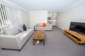 A living room with a grey sofa, a wooden coffee table, and a TV on a wooden stand. - Nelson Bay Ocean Jewel (Nelson Bay)