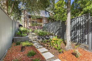 A pathway leading to a house with a brick exterior, surrounded by a metal fence and various plants. - Nelson Bay Ocean Jewel (Nelson Bay)