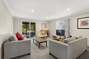 A modern living room with grey sofas, a coffee table, and a TV. - Nelson Bay Ocean Jewel (Nelson Bay)