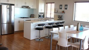 Eine moderne Küche mit weißen Schränken, einem Edelstahlkühlschrank, einer zentralen Kochinsel mit Barhocker und einem Esstisch mit Stühlen.
