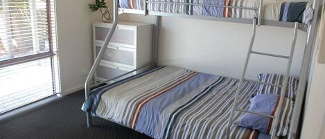 A bunk bed with striped bedding, a small white dresser, and a window with blinds.
