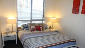 Ein Schlafzimmer mit einem Bett, zwei Nachttischen, einem Fenster mit Jalousien und zwei Wandlampen.