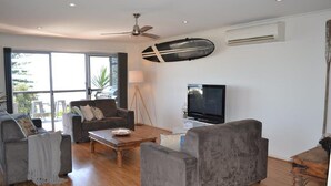 Ein Wohnzimmer mit einer Couch, Sesseln, einem Couchtisch, einem Fernseher und einem Deckenventilator.