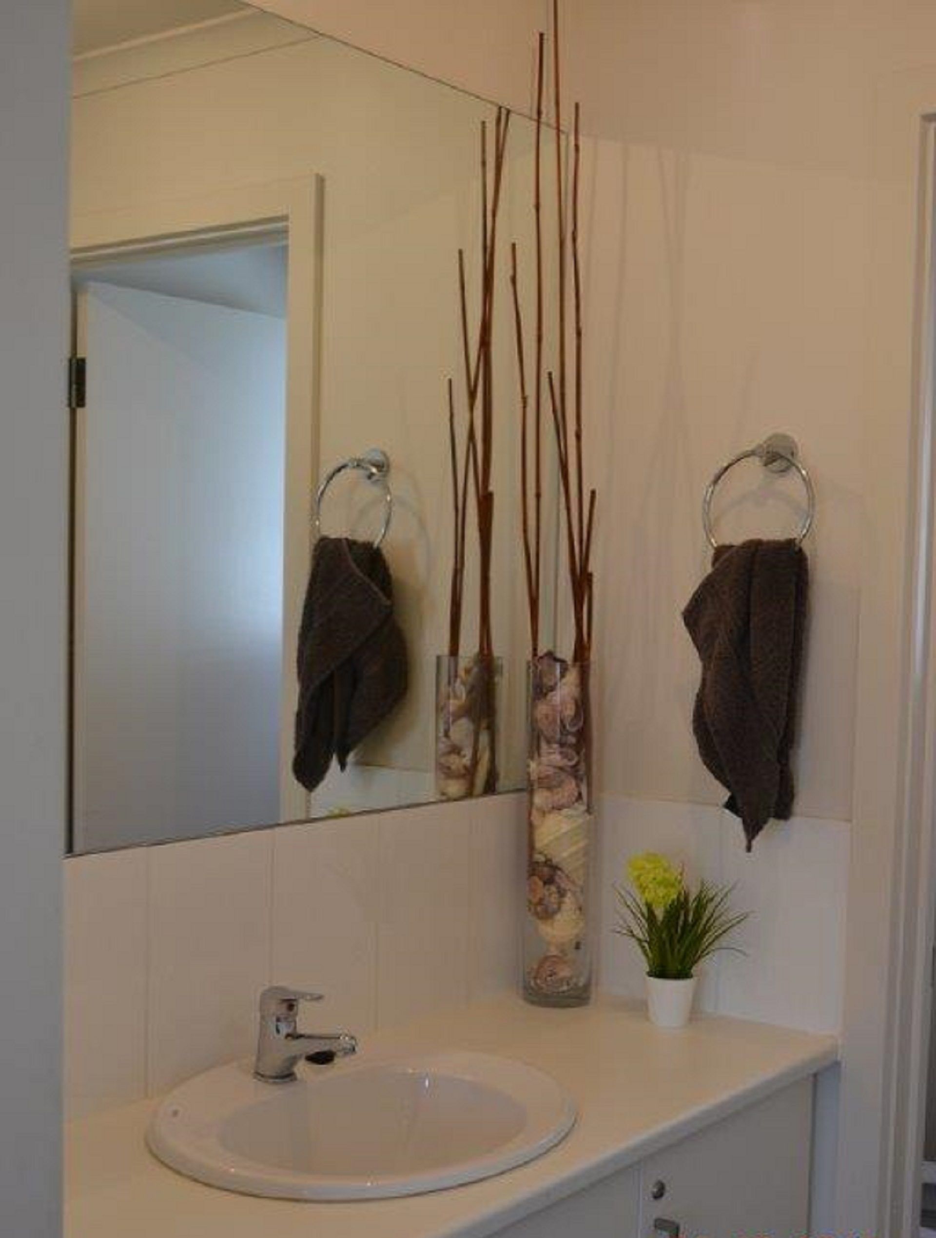 A bathroom with a white sink, a mirror, and two towels hanging on towel rings. There are decorative branches and a small plant on the counter.