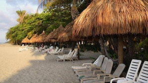 A beach with thatched umbrellas and white lounge chairs.