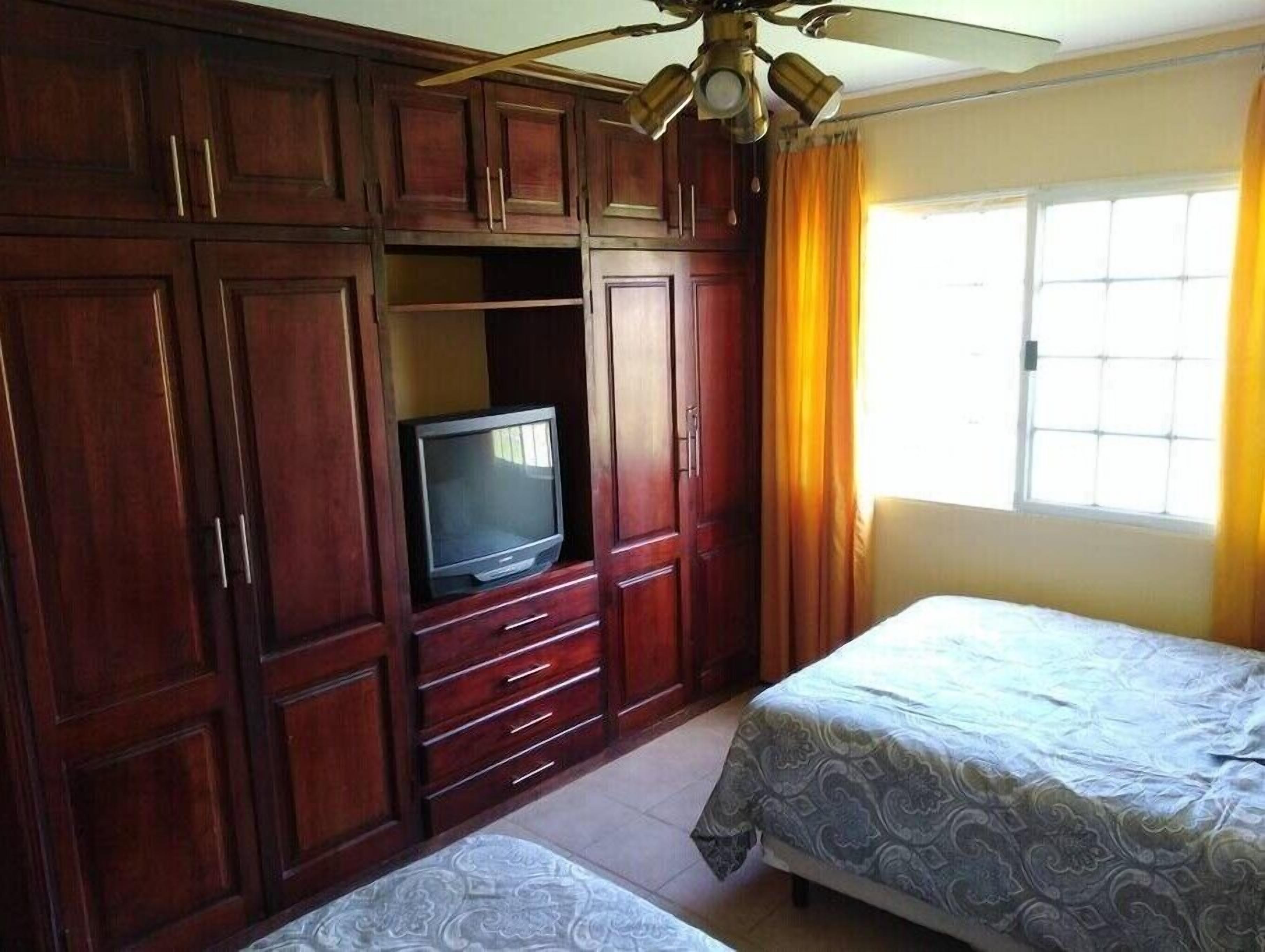 Una habitación con dos camas, un televisor sobre un mueble de madera y un ventilador de techo.
