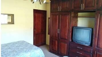 A bedroom with two beds, a wooden wardrobe, a ceiling fan, and a television.