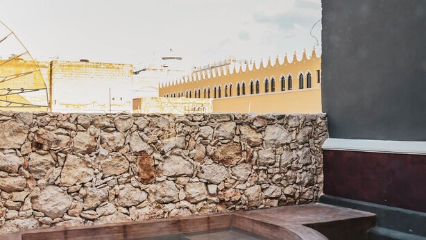 Un muro de piedra, un jacuzzi y un edificio con fachada amarilla al fondo.