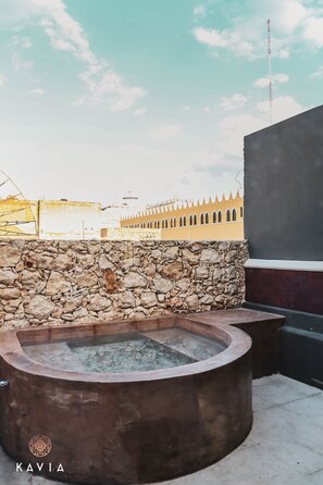 A stone wall, a hot tub, and a building with a yellow facade in the background. - Hotel Urban (Mérida)