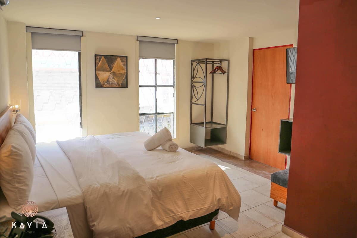 A hotel room with a bed, a wardrobe, a hanging wardrobe, a window, and a painting on the wall.