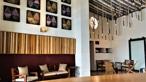 Un interior moderno con un mostrador de recepción de madera, una zona de estar con sillas acolchadas y una pared decorada con arte geométrico.
