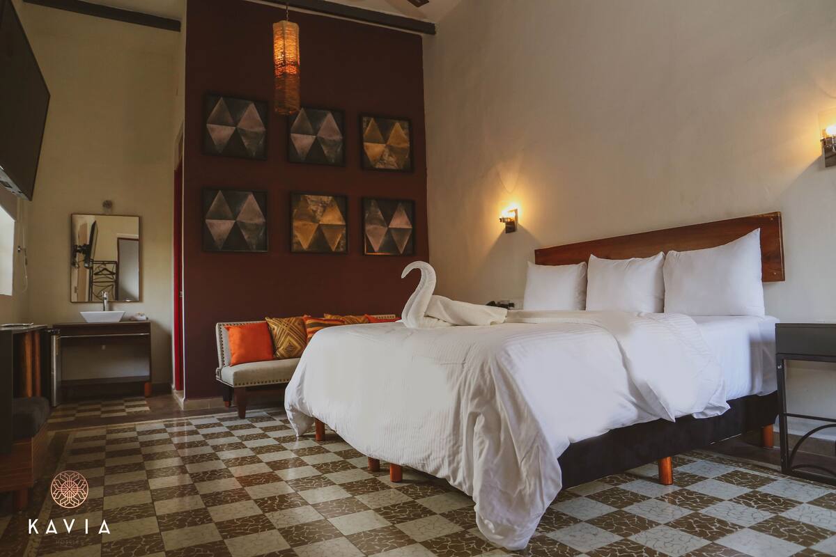 A hotel room with a checkered floor, a bed with white linens, a wooden headboard, and wall-mounted artwork.