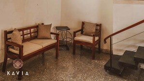 Una habitación con un banco de madera, una mesita, un florero y una ventana de cuadros.