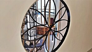 Una ventana circular con marco de metal y cuerdas, que da a una habitación con un sofá y un reposapiés estampado.