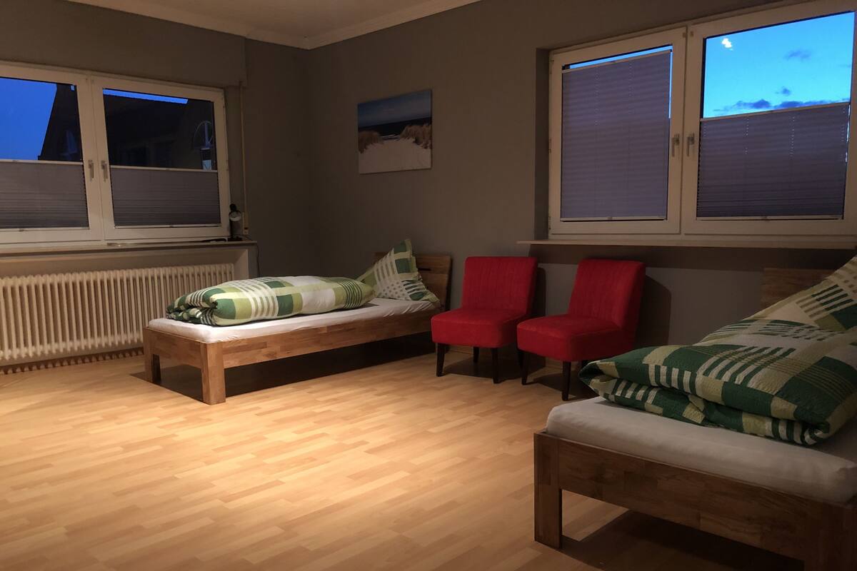Una habitación con piso de madera, una banca, una silla roja y un sofá con cojines estampados.