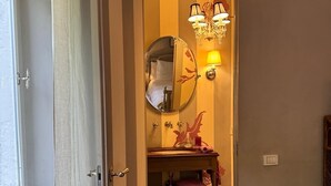 An open door leading to a bathroom with a mirror, a sink, a towel rack, and a small shelf with toiletries. - Florence Loft Duomo (Firenze)