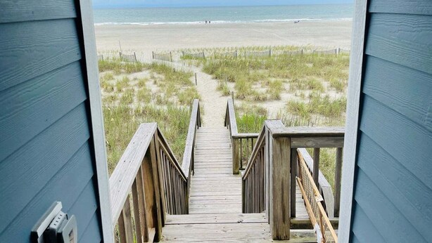 Une terrasse en bois qui mène à une plage et offre une vue dégagée sur l’océan.