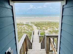 Une terrasse en bois qui mène à une plage et offre une vue dégagée sur l’océan.
