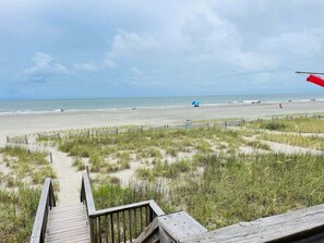 Une promenade en bois qui mène à une plage offrant une vue dégagée sur l’océan.