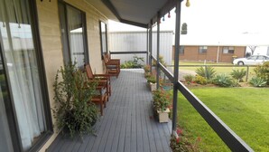 A covered outdoor area with wooden chairs and planters, a grassy lawn, and a building in the background. - Roshy's Retreat ~ sea views off deck - Off Peak Special! (Point Turton)