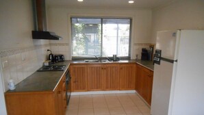 A kitchen with wooden cabinets, a white refrigerator, and a window with blinds. - Roshy's Retreat ~ sea views off deck - Off Peak Special! (Point Turton)