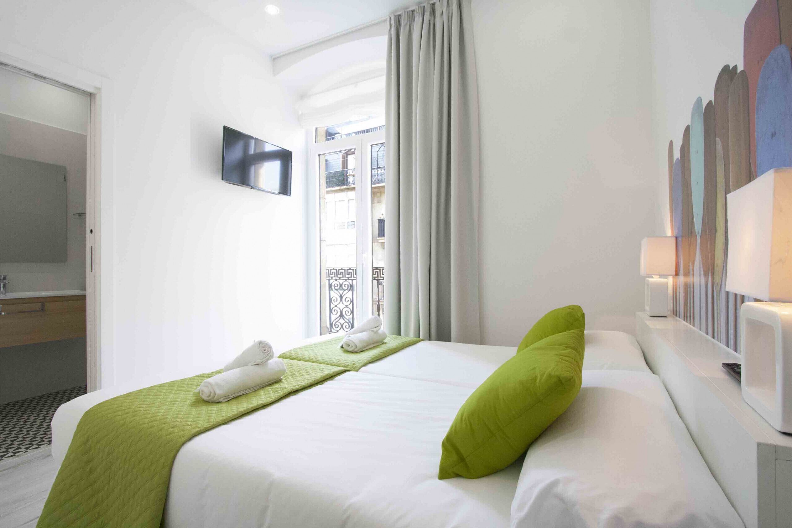 A hotel room with a bed, a TV, a window with curtains, and a balcony view.