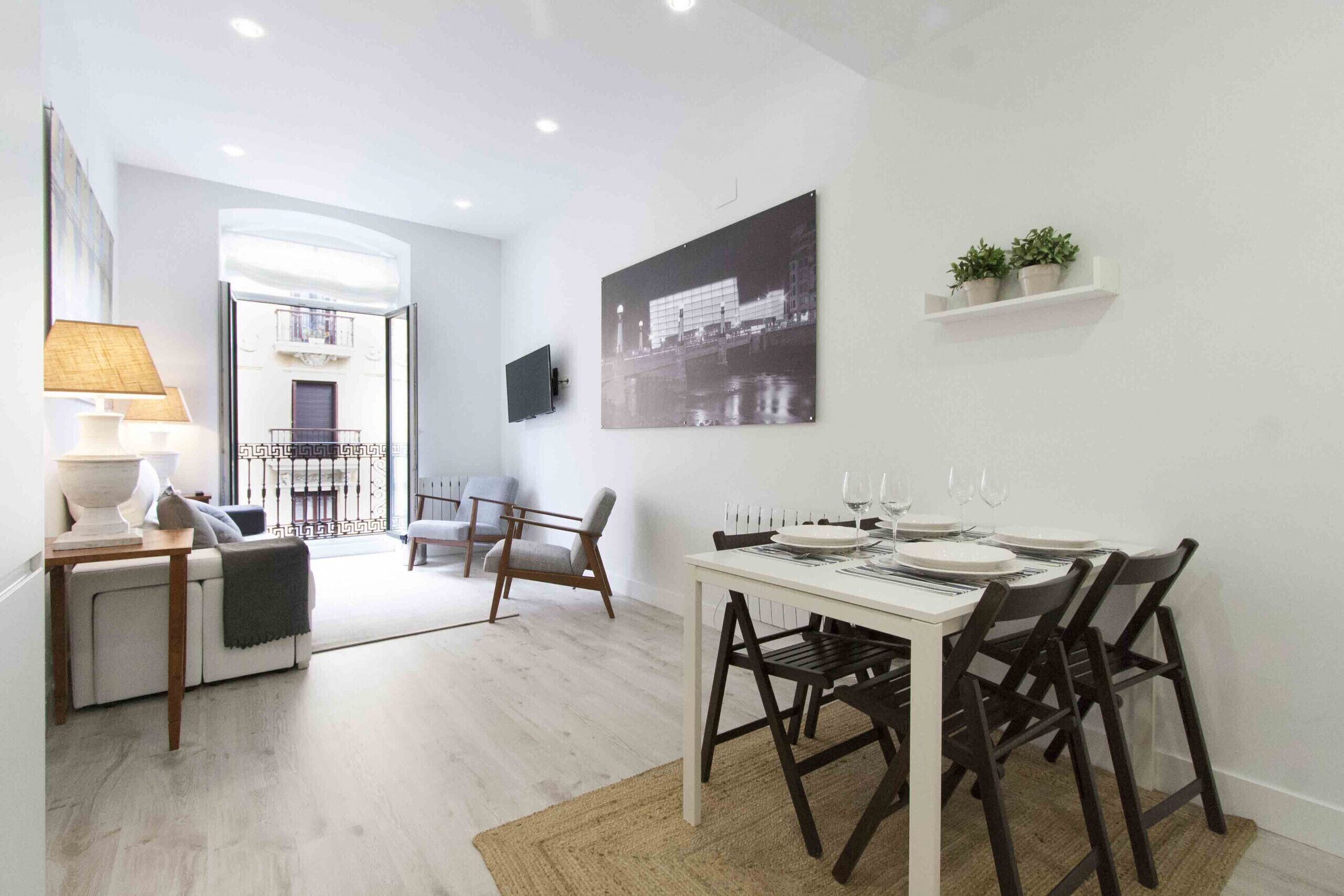 Een moderne eetruimte met een witte tafel gedekt voor vier personen, omringd door donkere stoelen. Een groot zwart-wit stadsgezichtsiers het schilderij boven de tafel.