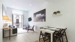 Un comedor moderno con una mesa blanca dispuesta para cuatro personas, rodeada de sillas oscuras. Un cuadro grande en blanco y negro de un paisaje urbano decora la pared sobre la mesa.