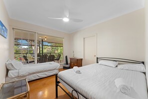 A hotel room with two beds, a ceiling fan, a window with a view of the outdoors, and a small table with chairs.