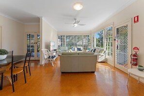 A spacious living area with a sofa, chairs, a dining table, and a ceiling fan.