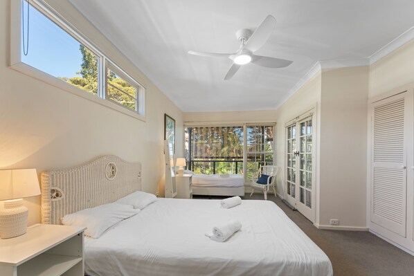 A bedroom with a bed, a bedside table, a lamp, a ceiling fan, and a window with a view of trees.