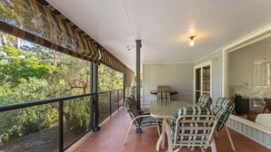 A covered patio with a table and chairs, a grill, and a view of the surrounding greenery.