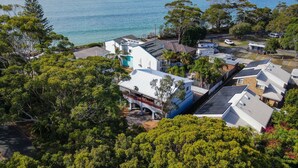 A residential area with houses, some with solar panels, surrounded by dense greenery and a view of the sea.