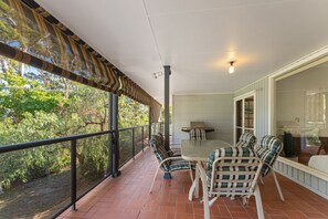 Een overdekt terras met een tafel, stoelen, een barbecue en uitzicht op de omliggende begroeiing.