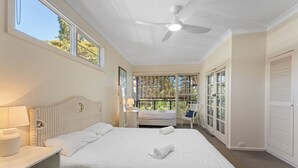 A bedroom with a bed, a ceiling fan, a window, and a chair.