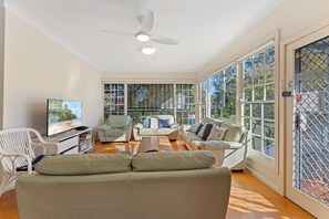 A spacious living room with a ceiling fan, large windows, and a television.