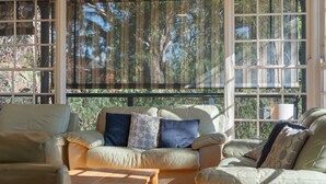 A sunlit room with a sofa, a small table, and large windows with a view of trees.