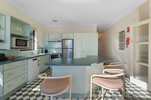 A compact kitchen with a central island, bar stools, a microwave, a refrigerator, and a sink.