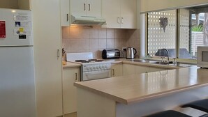 Cozinha equipada com fogão, micro-ondas e frigorífico. Há banquetas e uma janela com vista para o exterior.