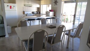 Uma cozinha moderna com armários brancos, uma mesa de jantar com cadeiras, uma geladeira e um micro-ondas.