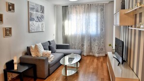 Un salon moderne avec un canapé gris, une table basse en verre, un téléviseur à écran plat et un plancher en bois.