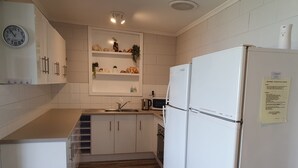Une cuisine moderne avec des meubles blancs, un four à micro-ondes encastré, un évier en acier inoxydable et un réfrigérateur blanc.