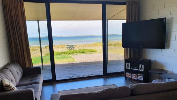 Un salon doté d’une grande porte-fenêtre coulissante donnant sur une terrasse avec vue sur la mer et une table de pique-nique.