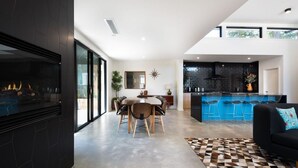 Eine moderne Küche mit einer blauen Bar, einem Essbereich mit großem Tisch und Stühlen, und einem Wohnzimmer mit schwarzem Sofa und gemustertem Teppich.