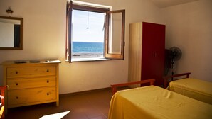 A room with a wooden dresser, a bed with a yellow bedspread, a red wardrobe, and a window with a view of the sea. - Ferruzzano portion of villa with stunning views and direct access to the sea (ferruzzano)