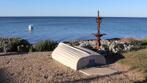 Ein Kiesstrand mit einer Betonbank und einer dekorativen Metallskulptur.