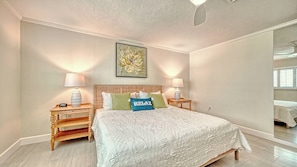 Quarto com uma cama grande, duas mesas de cabeceira, um criado-mudo, uma luminária na parede e um espelho.