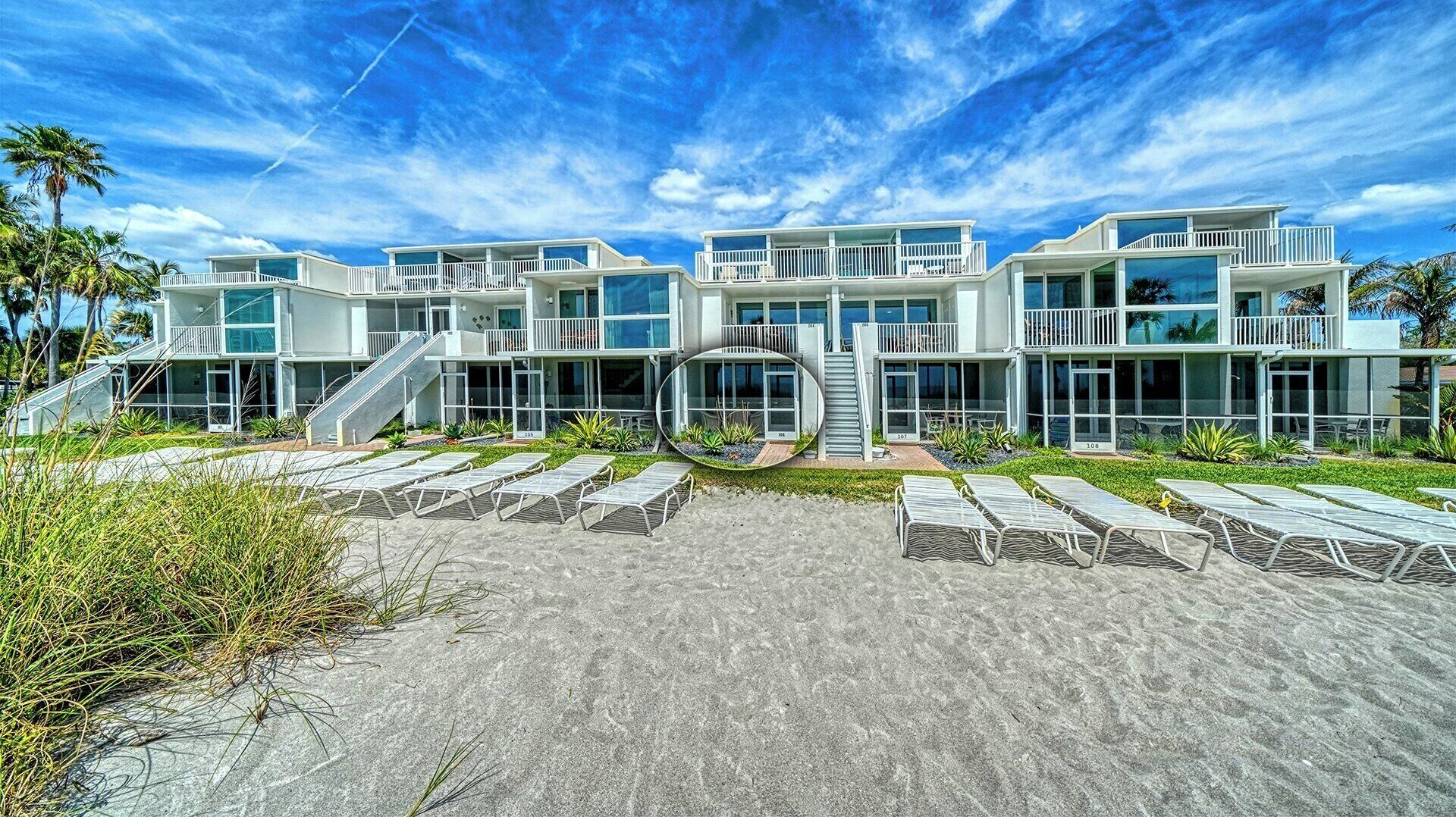 A modern beachfront hotel with multiple balconies, a central staircase, and sun loungers.