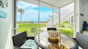 Un patio iluminado por el sol con muebles de mimbre, una mesa de vidrio y vista a la playa.